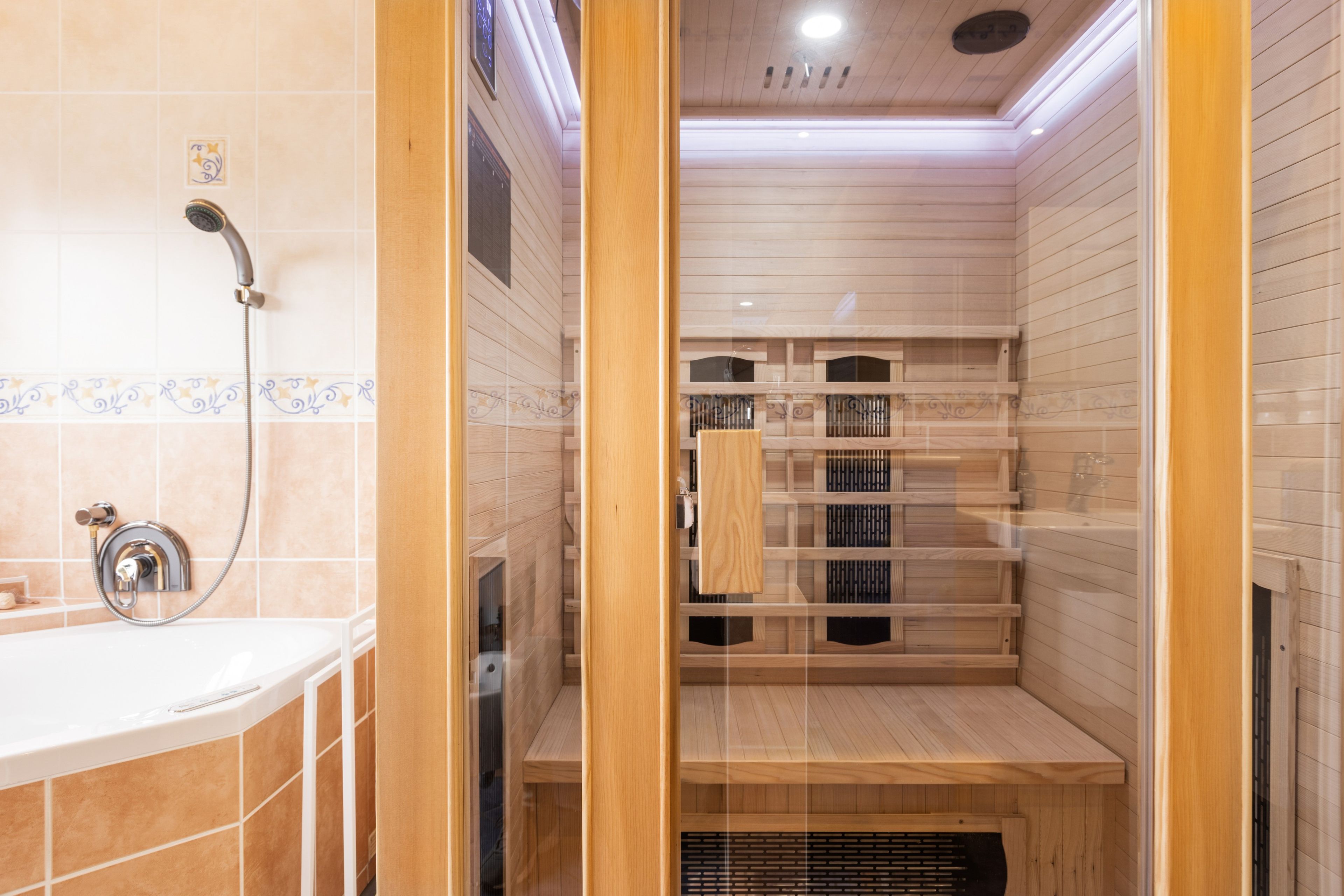 A modern bathroom with a glass-enclosed sauna area, a shower with a handheld showerhead, and a tiled wall with decorative patterns.