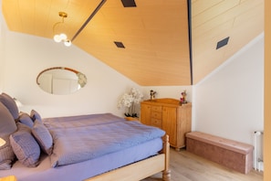 Un dormitorio con techo inclinado, una cama con manta azul, un aparador de madera y un espejo en la pared.