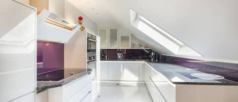 Une cuisine moderne dotée d’une verrière, de meubles blancs et de plans de travail en granit.