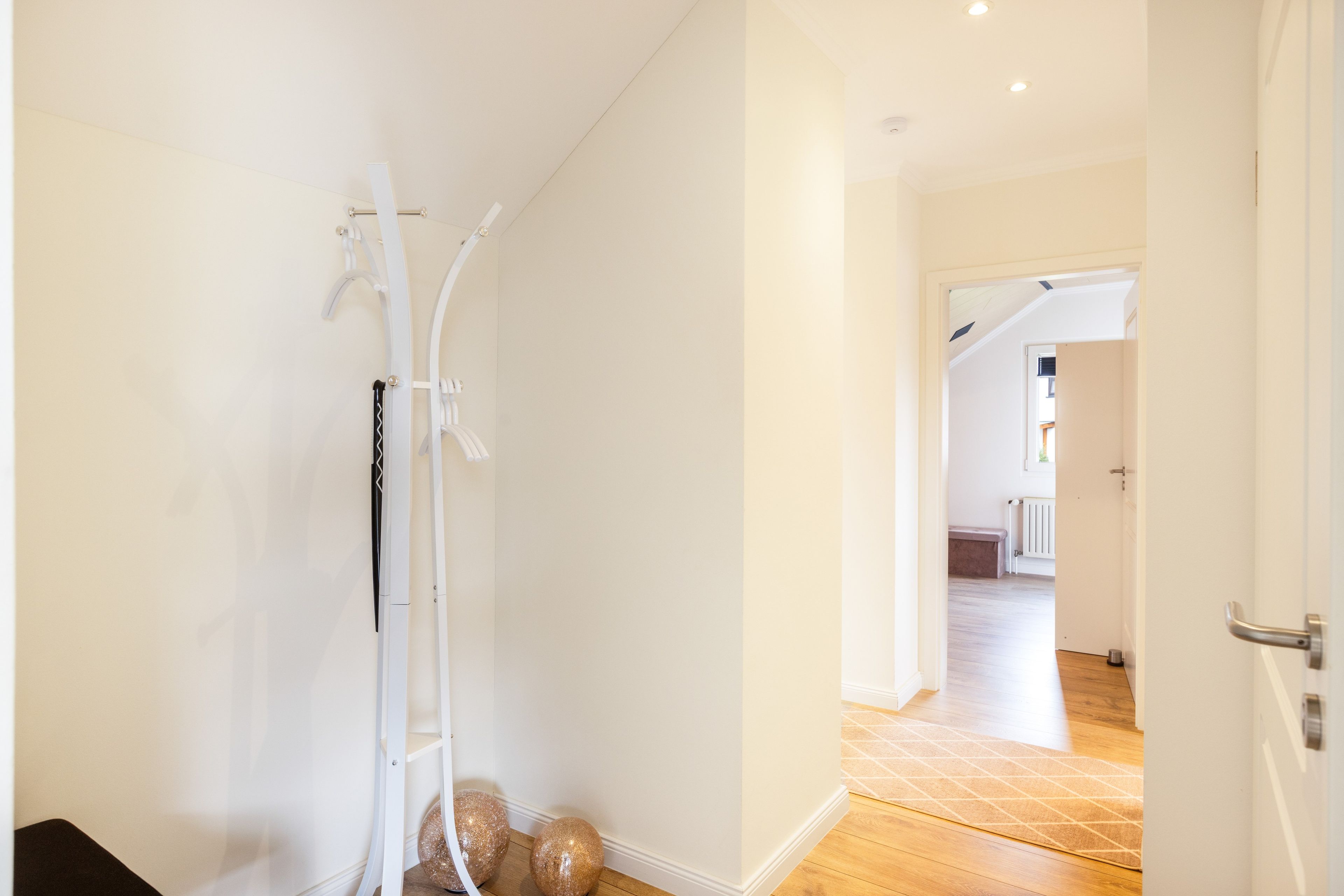 Un couloir avec un mur blanc, une porte blanche et un plancher en bois.