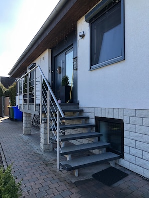A modern building with a staircase leading to a door, a small outdoor seating area, and a fire feature. - Apartment 'Am Wäldchen' with Shared Terrace, Shared Garden and Wi-Fi (Vöhl)