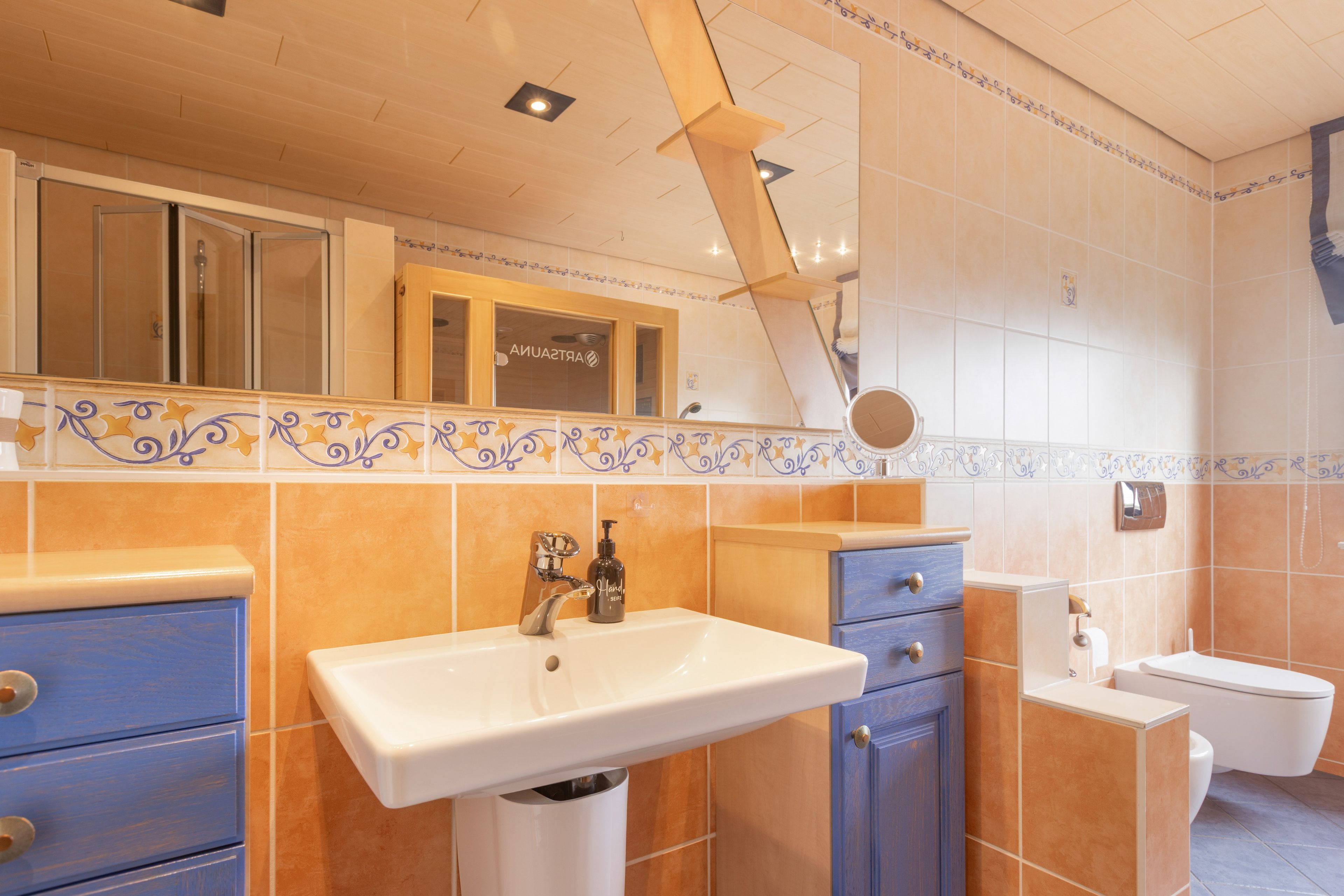 Un baño con un lavabo blanco, armarios azules, un inodoro y una zona de ducha.