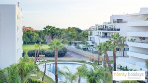A resort with a pool surrounded by palm trees and lounge chairs, modern architecture, and a view of other buildings in the background. - Ref. 567641 (Motril)