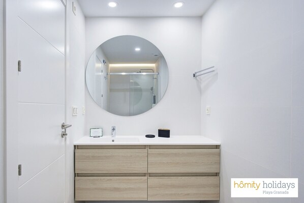 A modern bathroom with a white vanity, a round mirror, and a glass shower enclosure.