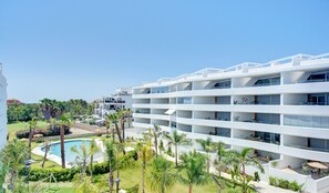 A modern hotel with multiple balconies, a swimming pool, and lush greenery.
