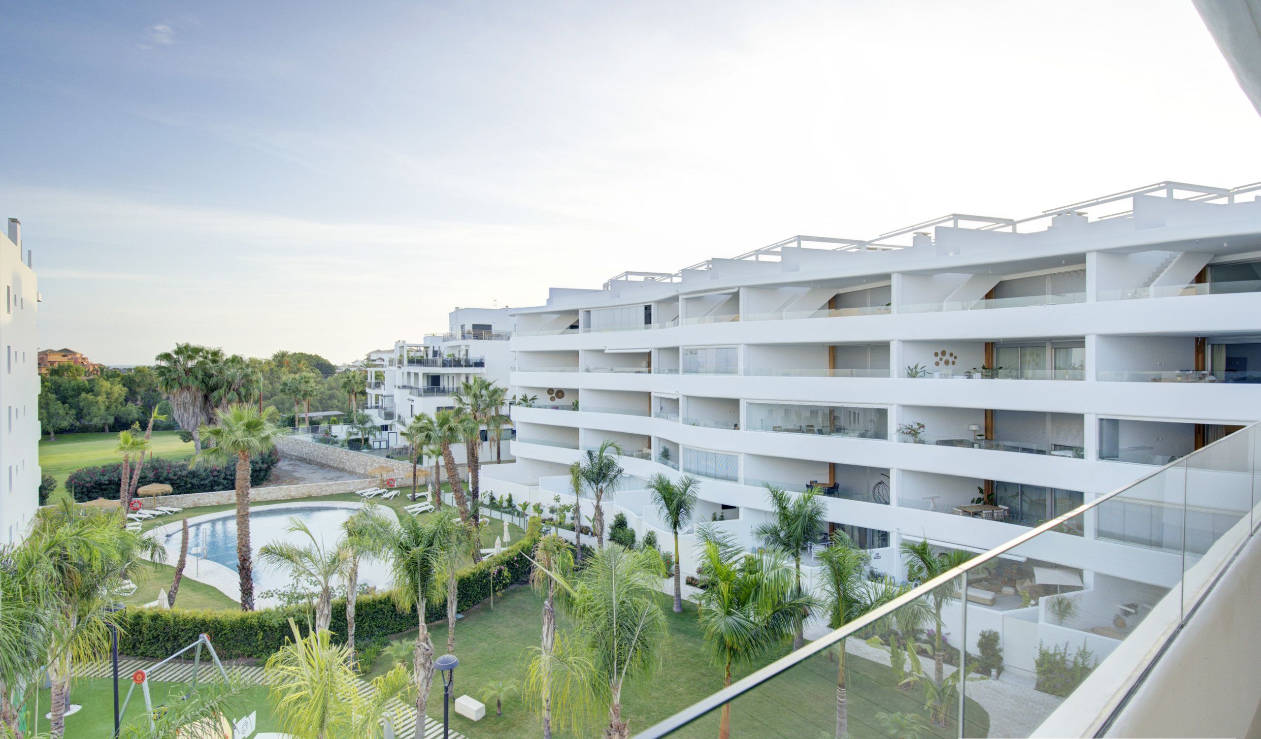 A modern hotel with multiple floors, a pool, and lush greenery.