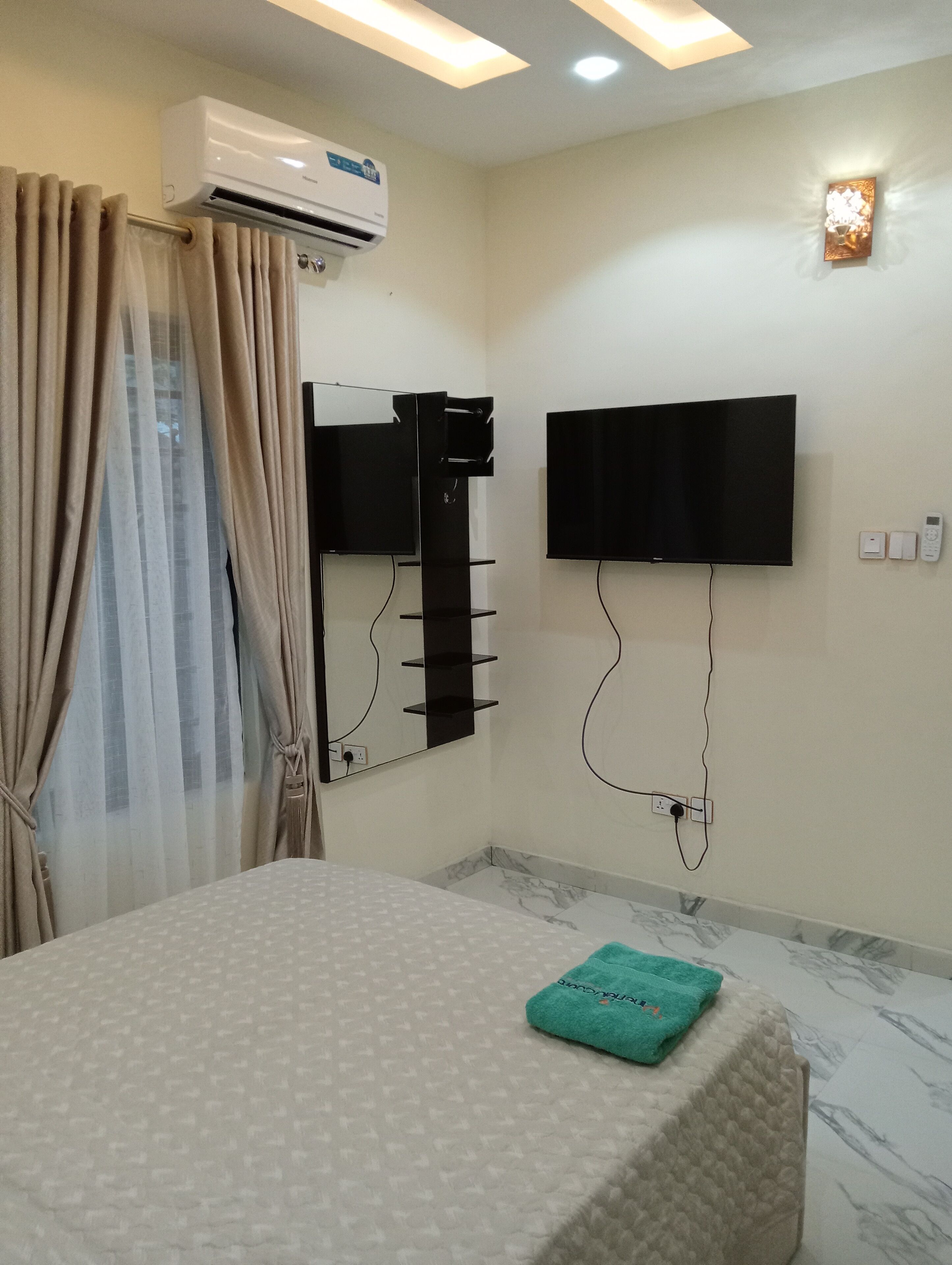 A hotel room with a bed, a mounted TV, a wall-mounted air conditioner, and a towel on the bed.