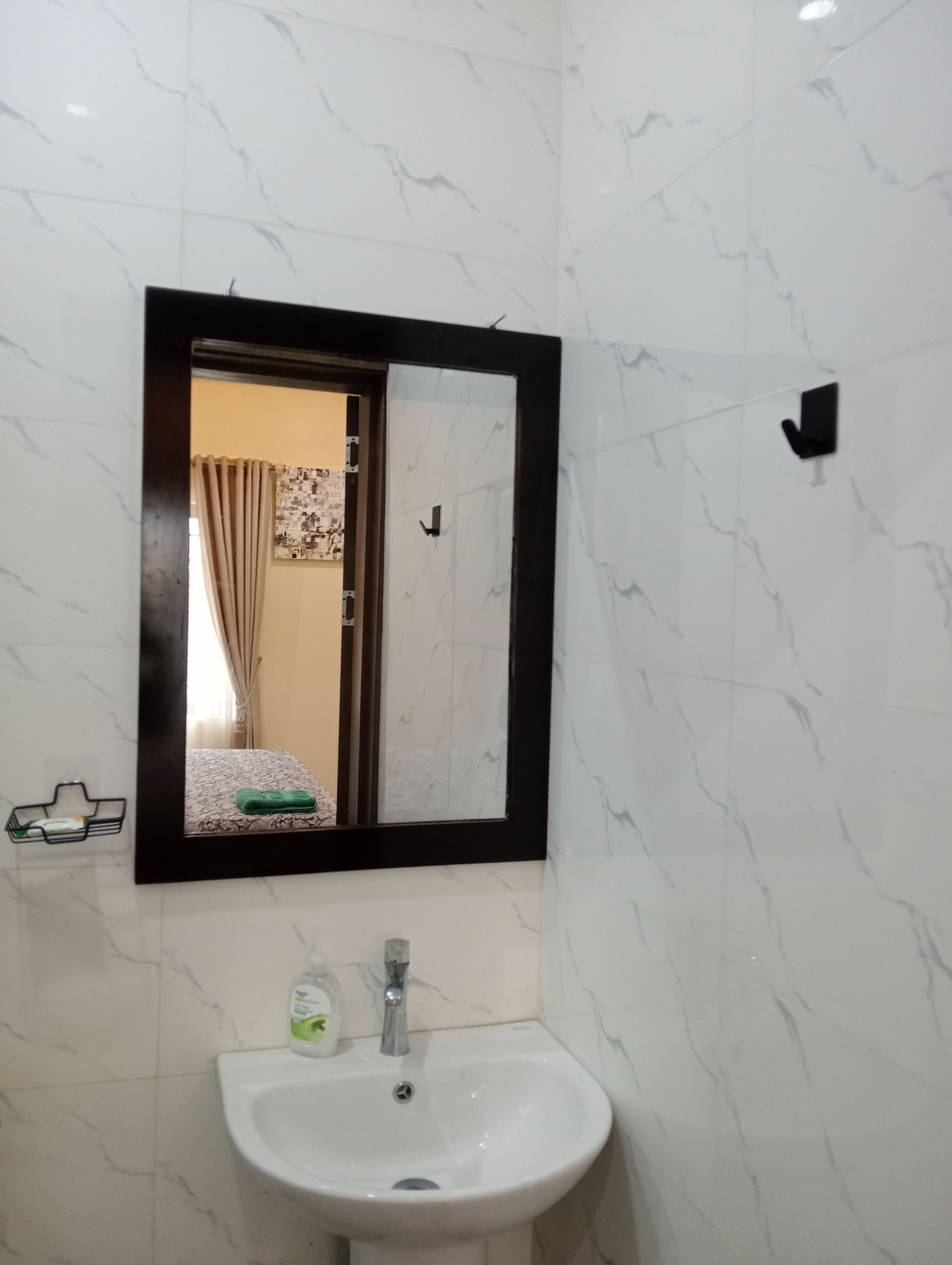 Un baño con pared de mármol blanco, lavamanos blanco con grifo, espejo con marco negro y toallero con toalla.