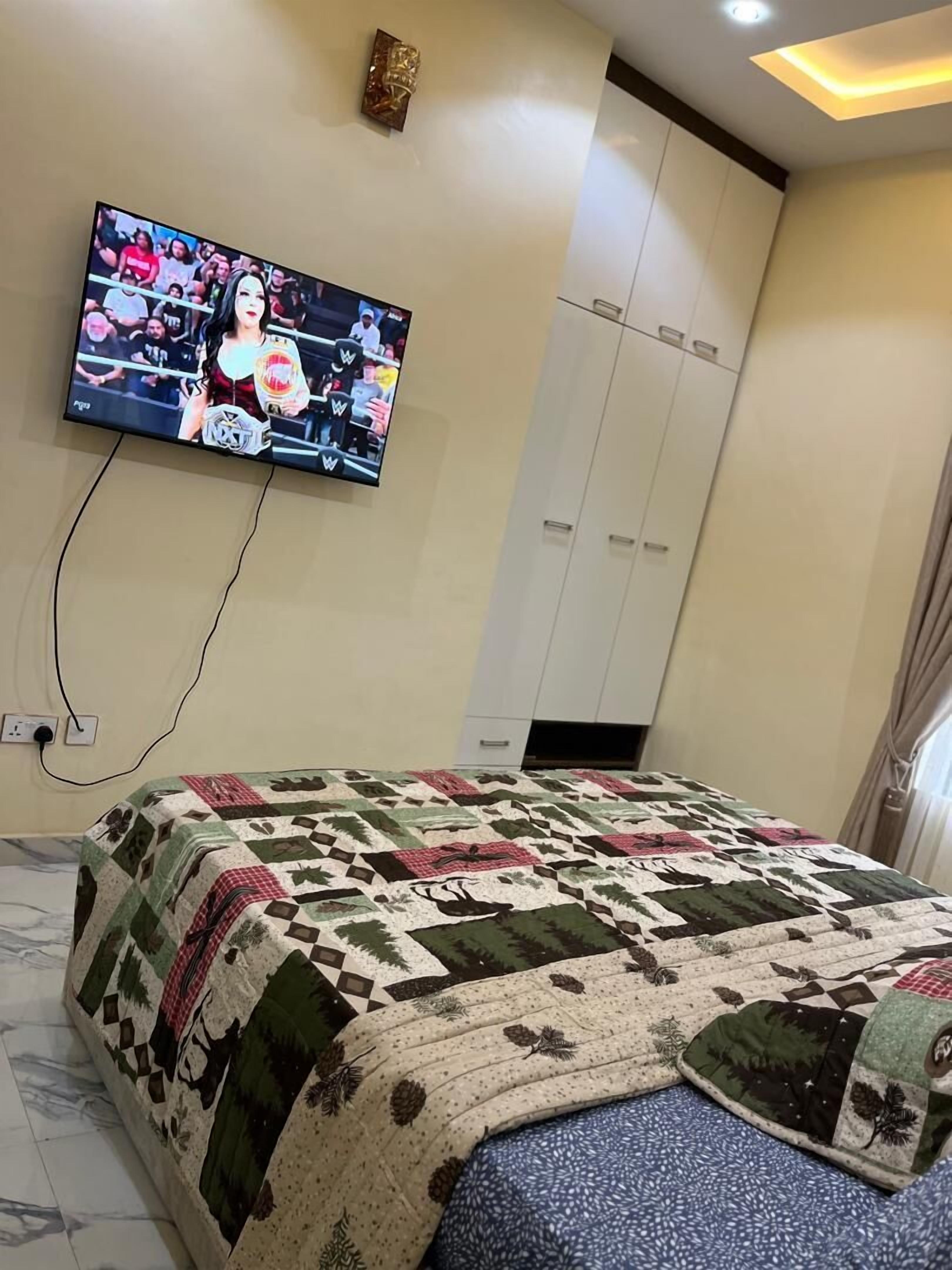 A bedroom with a large bed, a television mounted on the wall, and a wardrobe.