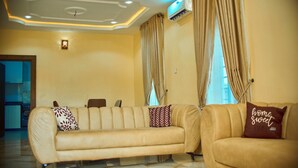 A living room with a beige sofa, two patterned pillows, and a 'home sweet home' pillow. - Pinefield Courts Apartmentl  (Akure)