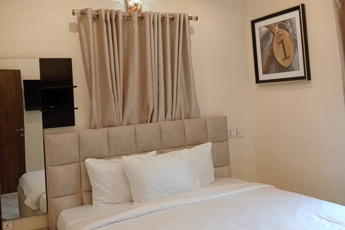 A neatly made bed with a headboard, a bedside table, a wall-mounted TV, and a framed picture on the wall.
