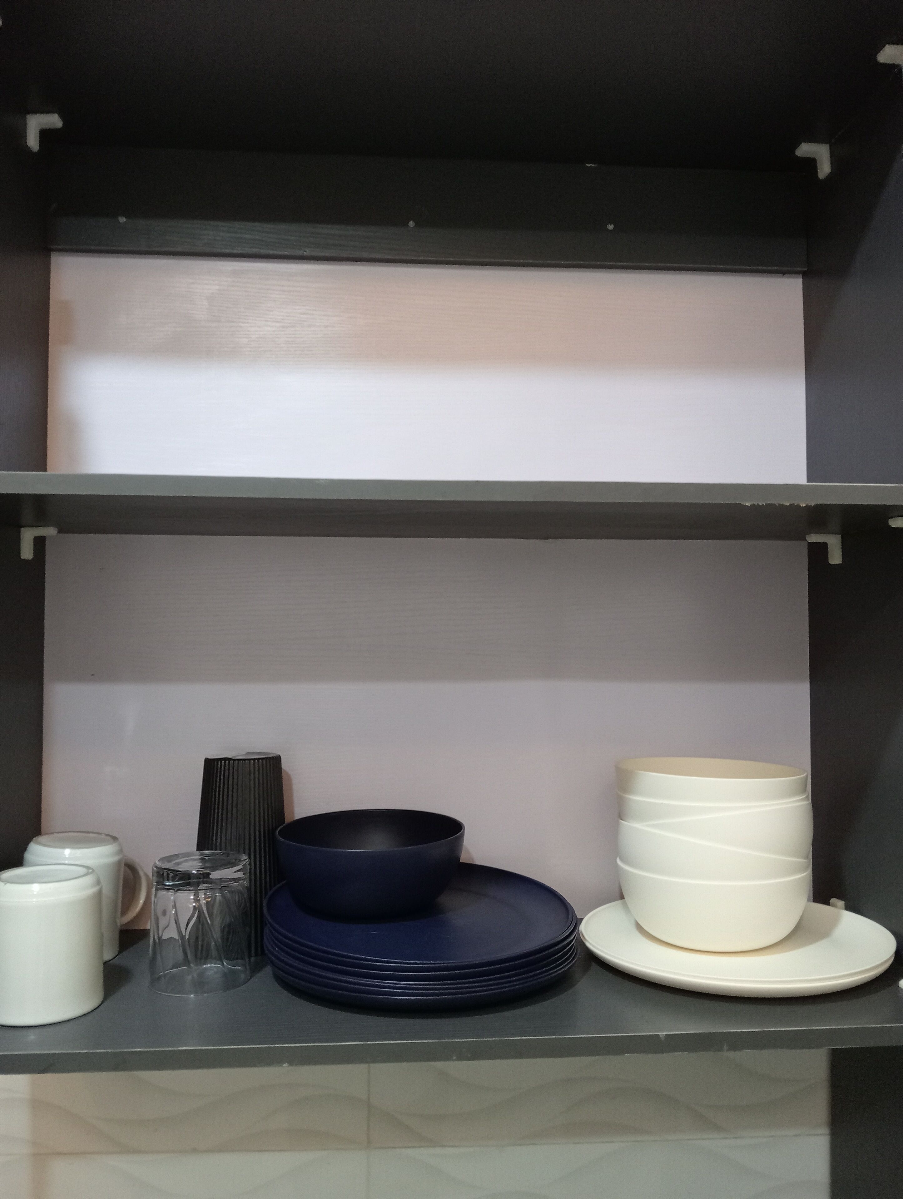 Een keukenschap met witte en blauwe borden, een glas en een witte container.