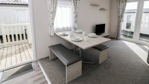 Un coin repas avec une table dressée pour quatre personnes, un banc, un téléviseur et une vue sur une terrasse extérieure.