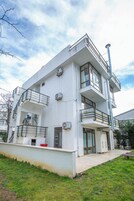 Un edificio de varios pisos con balcones, unidades de aire acondicionado y un área de entrada pavimentada.