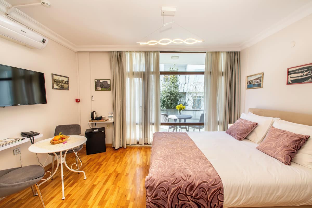 A hotel room with a bed, a desk, a chair, a TV, and a balcony with a table and chairs.