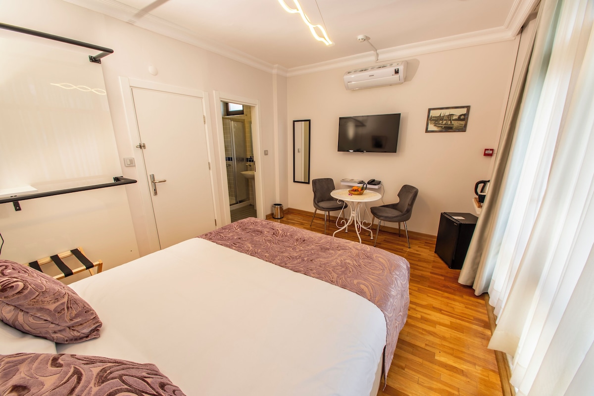 Una habitación de hotel con cama, televisor, escritorio con silla y una pequeña mesa con otra silla.