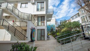 A multi-story building with a staircase, a mural, and a garden area. - Poseidon Kinaliada Pansiyon (Adalar)