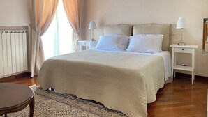 A neatly arranged bedroom with a bed, two bedside tables with lamps, a radiator, and a window with curtains.