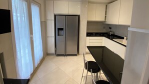 A modern kitchen with white cabinets, a stainless steel refrigerator, a black countertop, and a black chair.