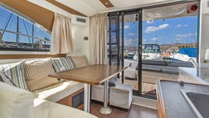 Interni di uno yacht con zona pranzo, posti a sedere e vista sul porto turistico.