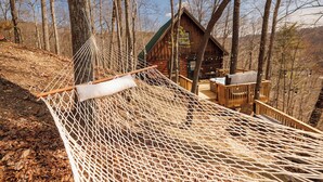 A hammock in a forested area with a cabin in the background.