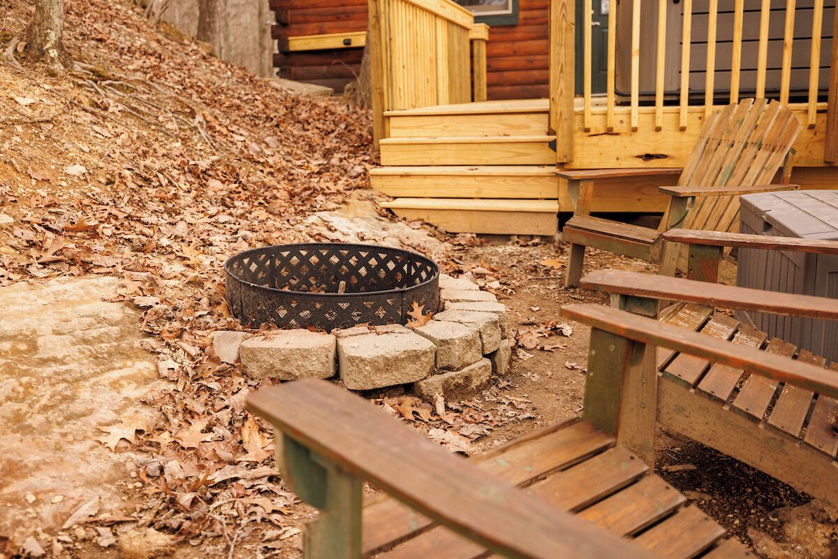A wooden deck with a fire pit, wooden steps, and Adirondack chairs.