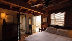 A bedroom with a wooden ceiling, a bed, a nightstand, a lamp, and a window with blinds.