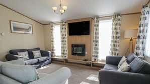 Una sala de estar con dos sofás, un televisor de pantalla plana, una chimenea y cortinas estampadas.