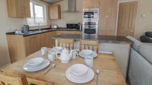 Cocina compacta con armarios de madera, horno integrado y comedor con vajilla blanca y una mesa.