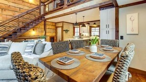 Un'ampia sala da pranzo con un tavolo di legno apparecchiato per quattro persone, circondato da sedie di vimini. Una scala con ringhiera in legno conduce a un piano superiore.