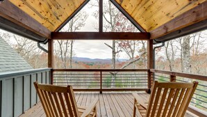 Un pontile in legno con due sedie e una ringhiera, affacciato su un paesaggio montuoso con foglie autunnali.