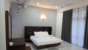Une chambre d’hôtel moderne avec un grand lit, une table de chevet en bois, un miroir et un ventilateur de plafond.