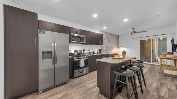 A modern kitchen with dark cabinets, stainless steel appliances, and a central island with bar stools.