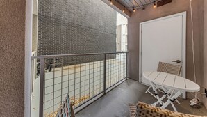 A balcony with a white table and chairs, a metal railing, and a view of a brick building.