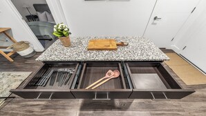A kitchen area with a granite countertop, a wooden cutting board, and a drawer organizer containing kitchen utensils.