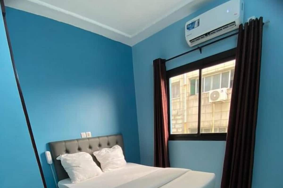 A bedroom with a bed, a desk, and an air conditioning unit.