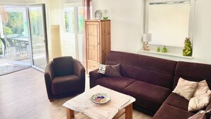 Una sala de estar con un sofá marrón, una silla, una mesita con un plato, un mueble de madera y una ventana con persianas.