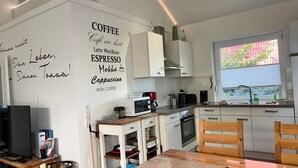 Una cocina moderna con armarios blancos, una mesa de comedor de madera y una pared con texto alusivo al café.
