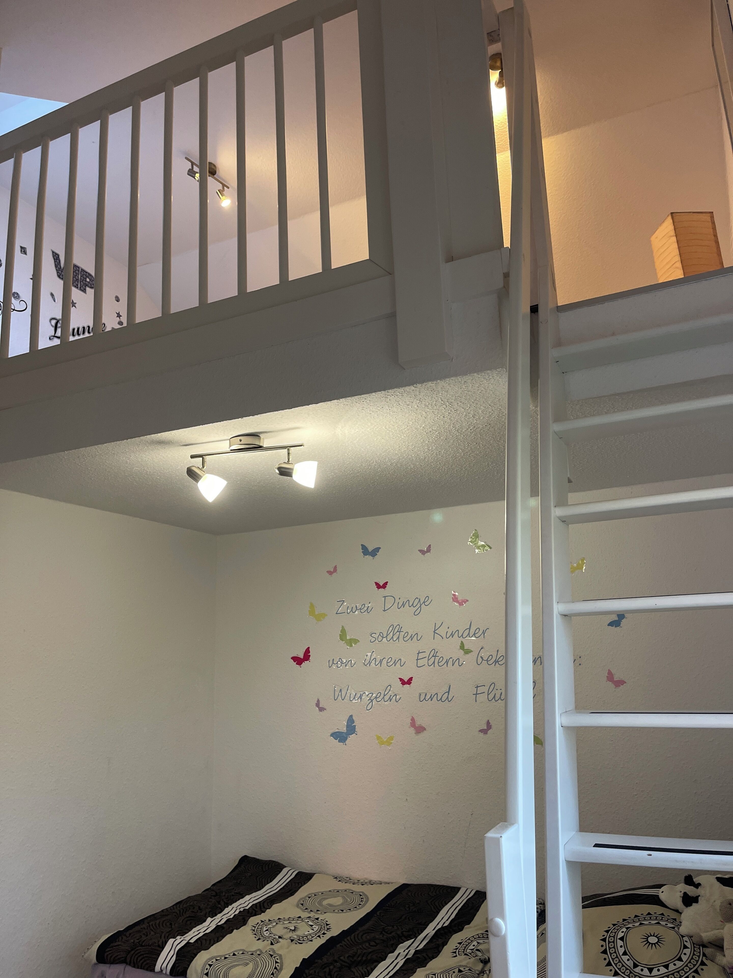 A child's bedroom with a bunk bed, a wall with butterfly decals, and a ceiling light fixture.