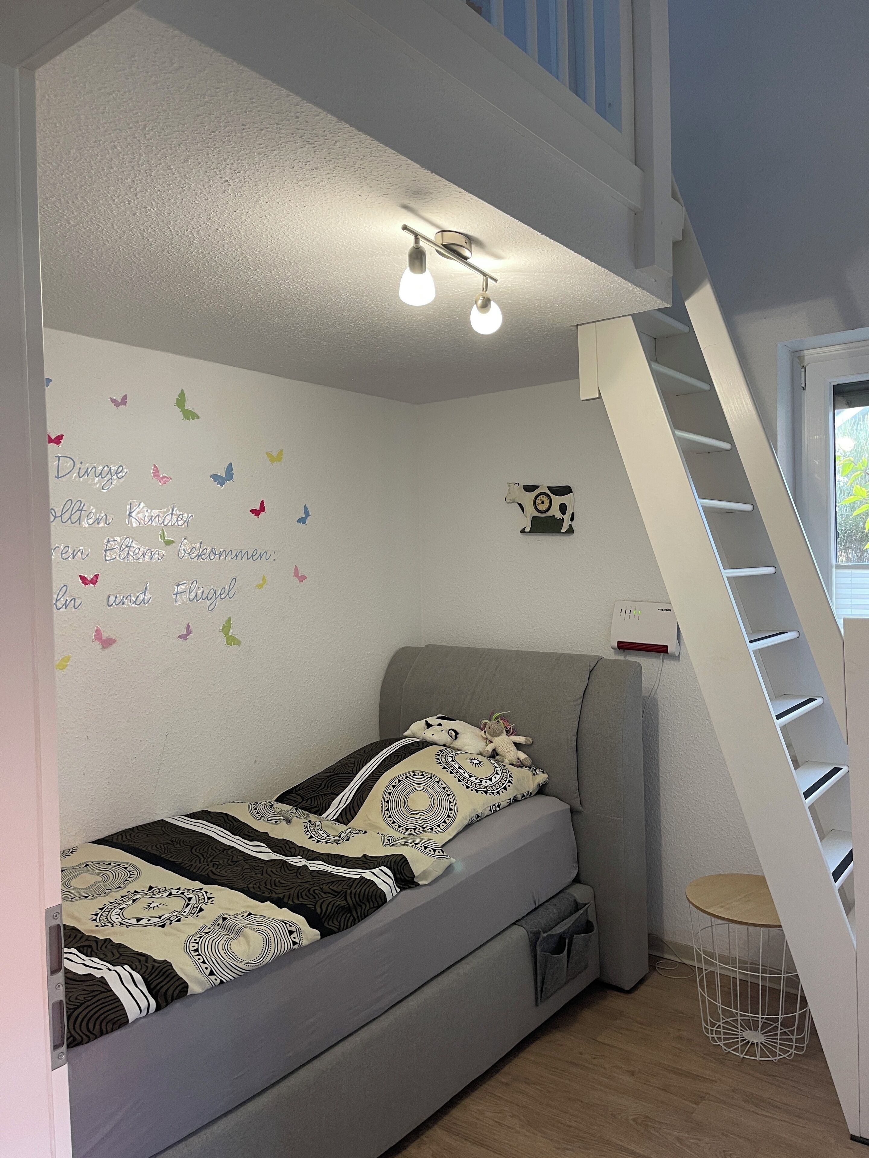 A bedroom with a bunk bed, a wall-mounted shelf, a small table, and a window with blinds.