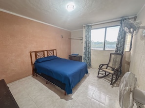A bedroom with a bed, a chair, a small table, and a window with curtains.