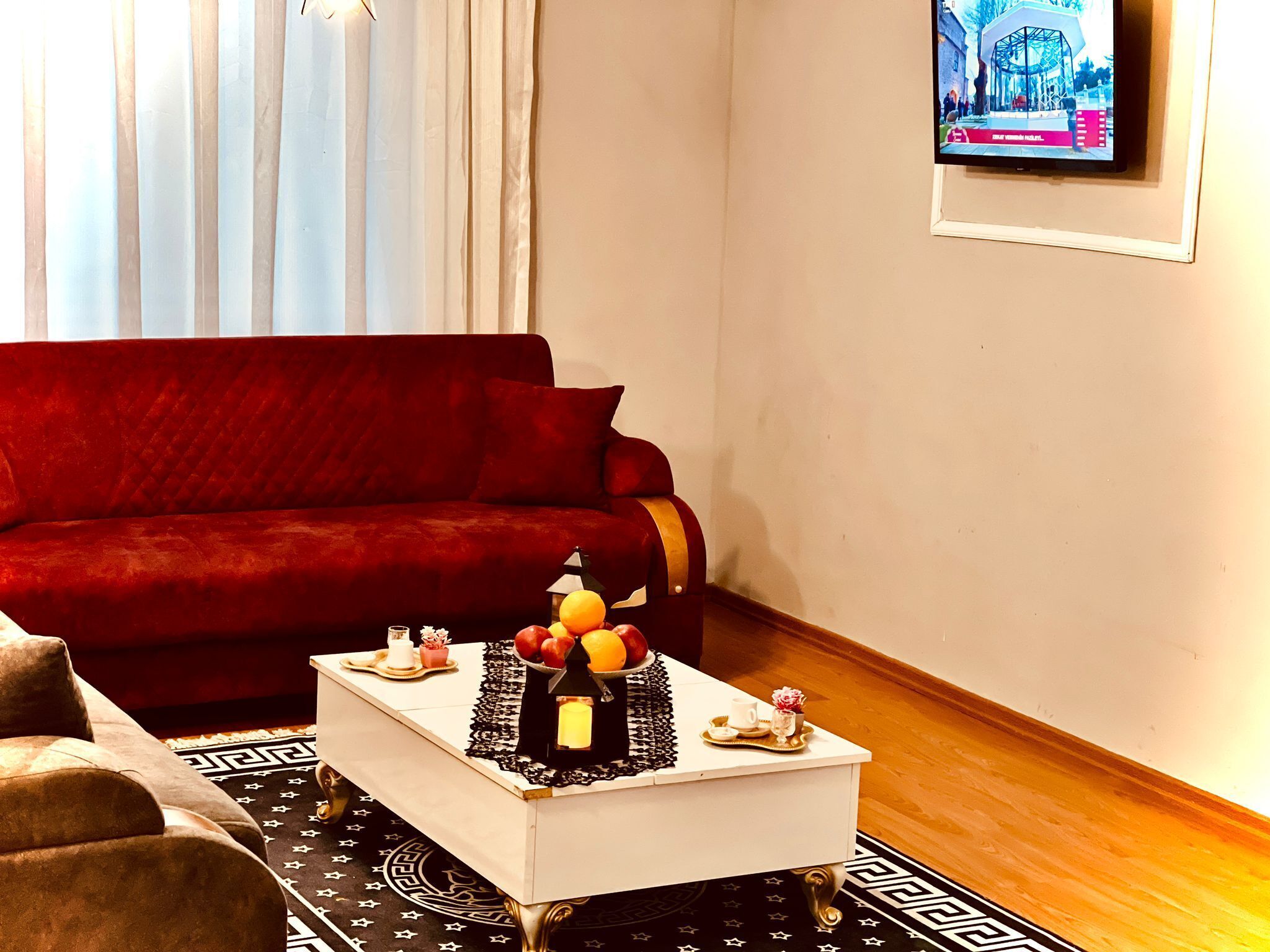 Una sala de estar con un sofá rojo, una mesa de centro blanca con adornos y un televisor en la pared.