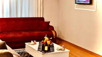 Una sala de estar con un sofá rojo, una mesa de centro blanca con adornos y un televisor en la pared.