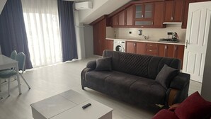 A living room with a sofa, a coffee table, a dining table with chairs, a kitchen area with cabinets and appliances, and a window with curtains. - Bagdad Apart (Ordu)