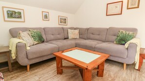 A living room with a grey sofa, a wooden coffee table, and framed pictures on the wall. - Five Elements Barn (Truro)