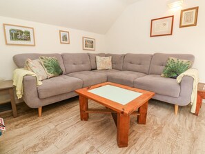 A living room with a grey sofa, a wooden coffee table, and framed pictures on the wall. - Five Elements Barn (Truro)