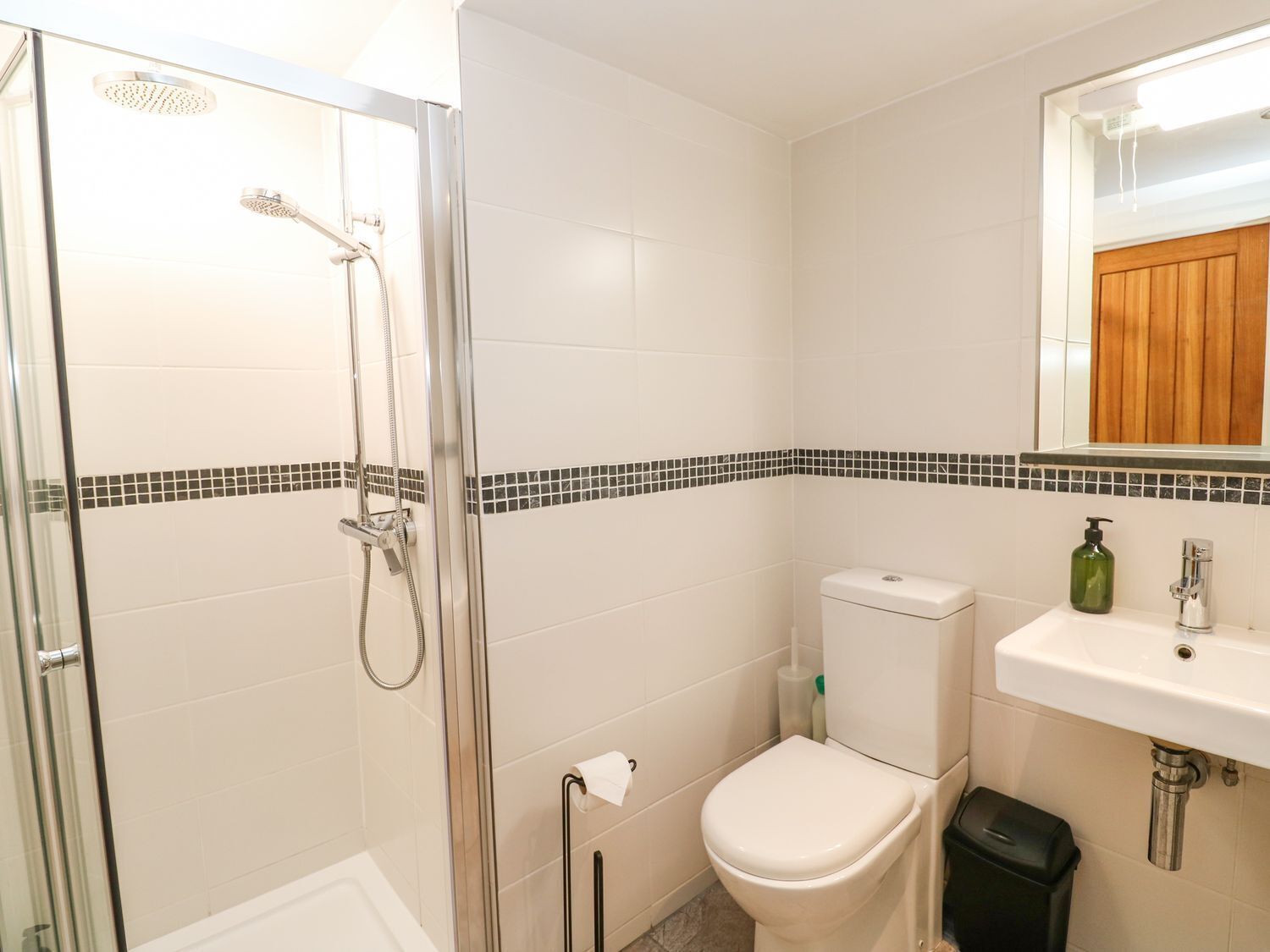 Et badeværelse med bruseniche, toilet, håndvask og spejl.