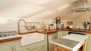 A compact kitchen with a sink, dishwasher, and a small dining area with a table and chairs. - Five Elements Barn (Truro)