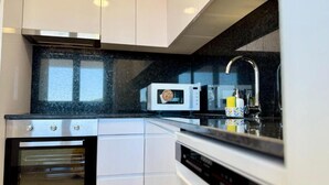 A modern kitchen with white cabinets, a black countertop, a built-in oven, a microwave, and a stainless steel faucet. - Cíes Suitel Prado (Nigrán)