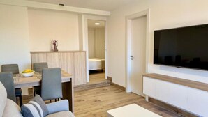 A modern living room with a flat-screen TV mounted on the wall, a dining area with a wooden table and chairs, and a hallway leading to a bedroom. - Cíes Suitel Prado (Nigrán)